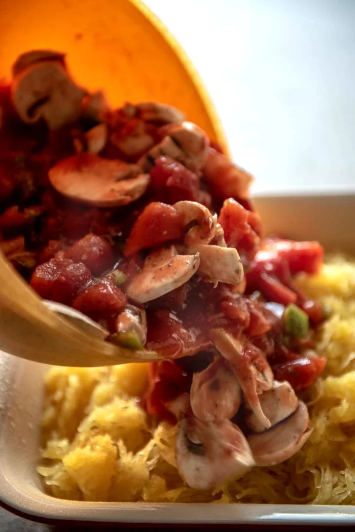 pouring chicken and vegetables over spaghetti squash for a casserole