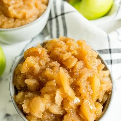 A close up image of chunky applesauce with green apples in the background