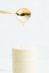 Small mason jar of sweetened condensed milk under a dipped gold spoon.